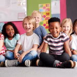 Portrait Of Elementary School Pupils Sitting On Floor In Classroom